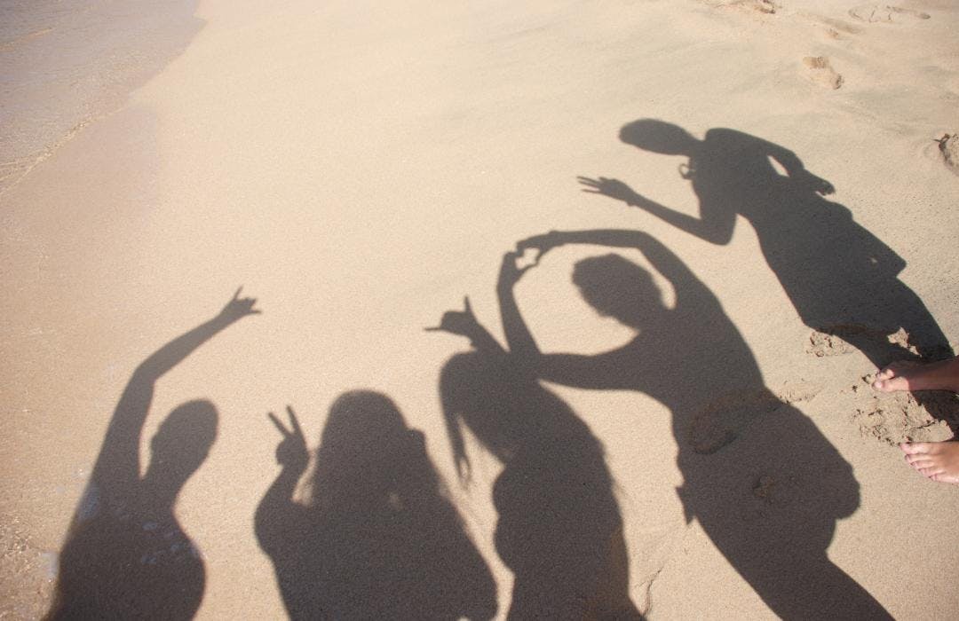 Group photo of people's shadows on a sunny beach, holding their hands in peace and love signs